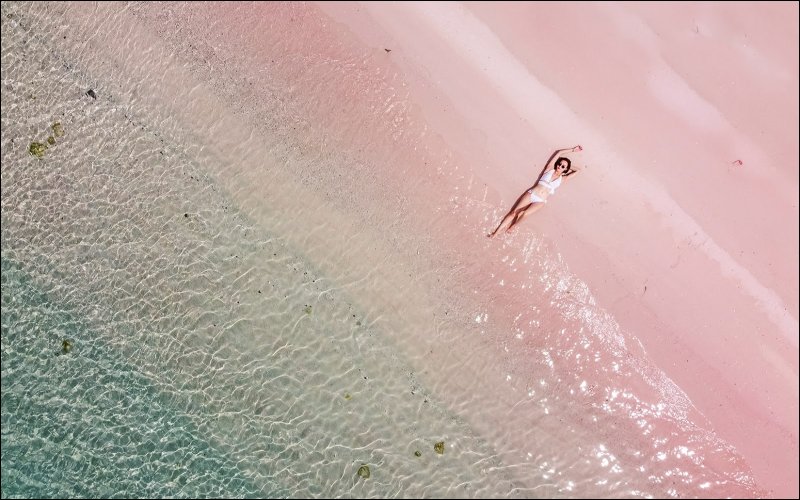 Girl in white bikini posing on pink sand beach with ocean waves in the background, Harbour Island."